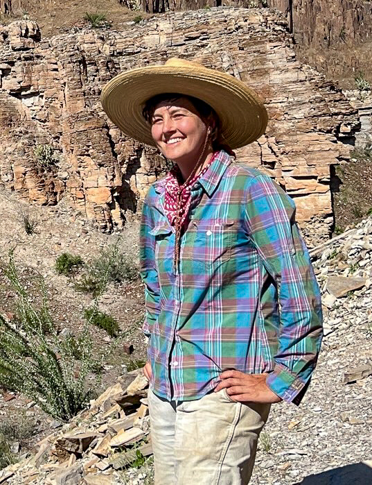 photograph of smiling woman standing in the desert wearing a big hat