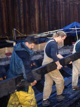 photo of crew moves one of the heavy timbers disassembled from the hull to the water vat area