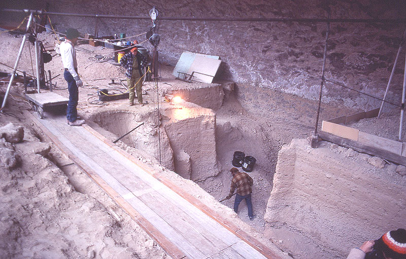 View looking grid northeast early on in 1983 season into the main excavation block. Bucket hoist in place along with wooden track and dirt trolly. Crew member is shoveling out overburden. Photo by Jack Skiles.