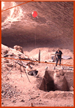 Curtis Tunnel (at plane table) and Elton Prewitt (seated) use red weather balloon to plot height of shelter ceiling.  View due grid north along W30 of northernmost excavation block in central area of shelter. Photo taken on February 20, 1964, probably by 