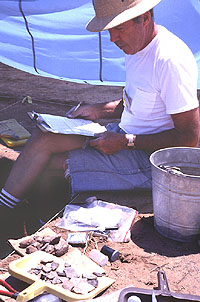 Excavator looks over the artifacts just found as he prepares field notes.