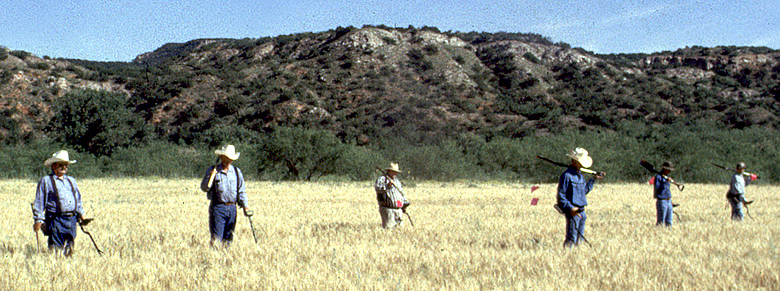 photograph of people lined up in a field with rocky hills behind them