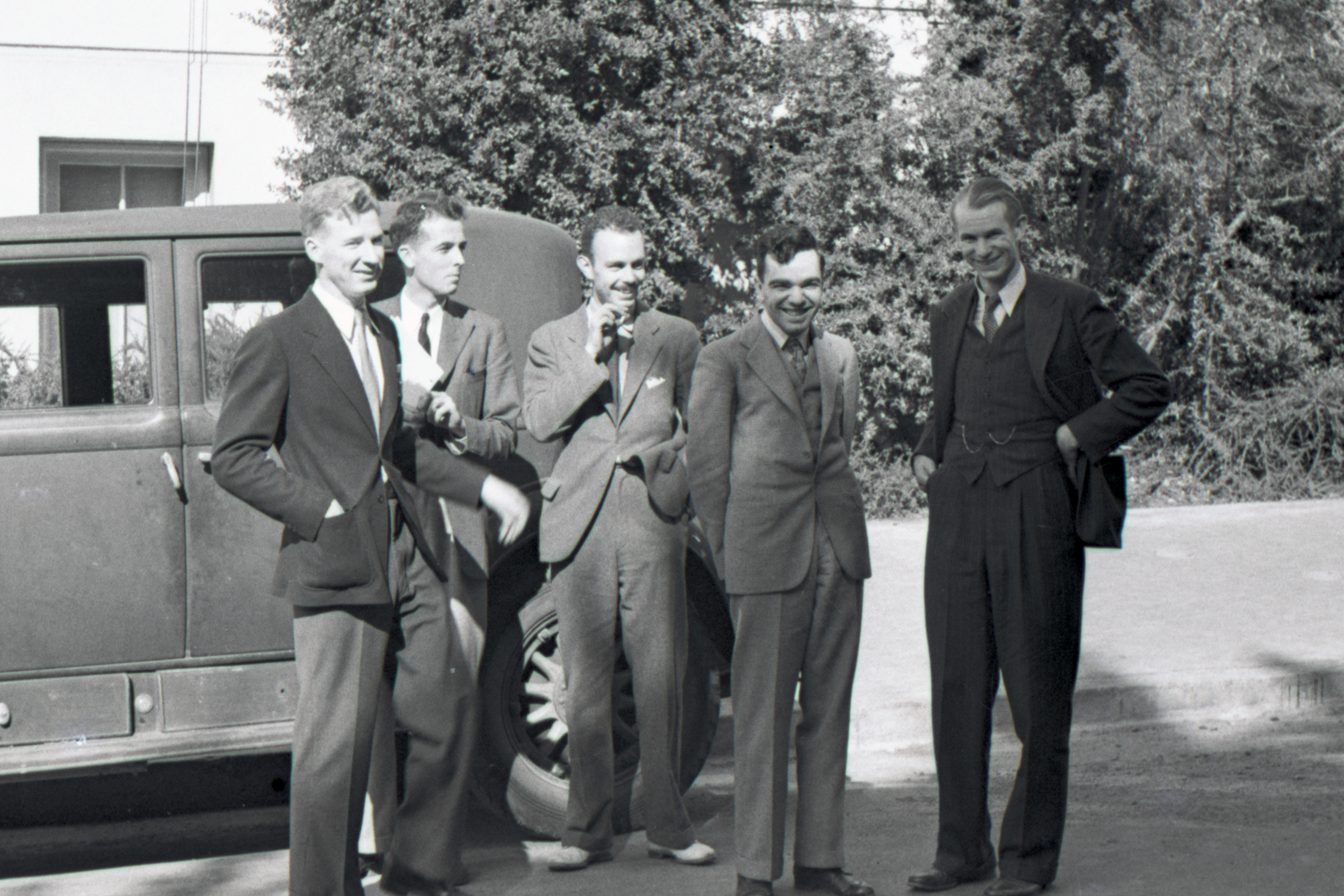 Black and white photograph of five men standing outside near a car