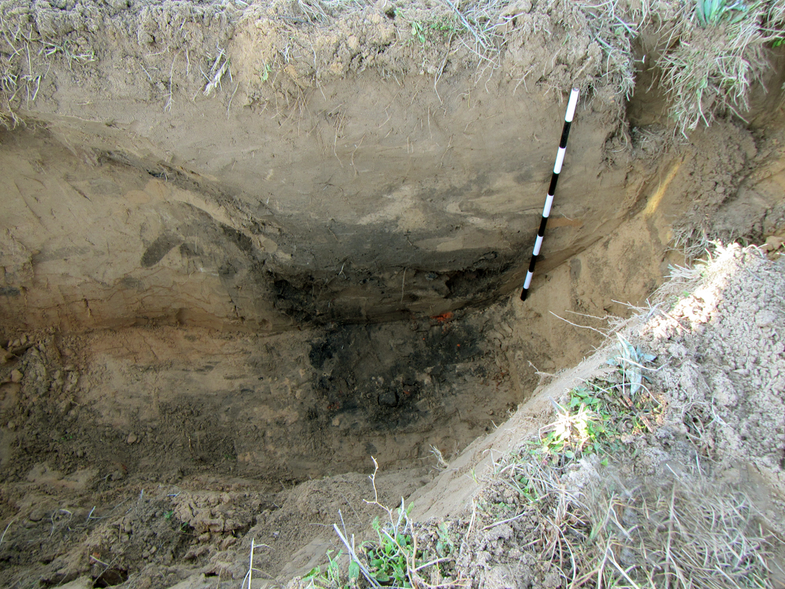 photo looking down into deep trench wall, at the base of which is a dark colored pit