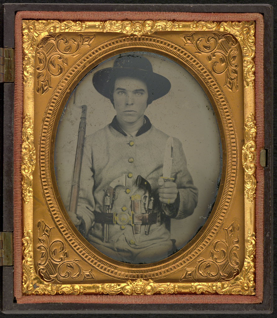 A hand-colorized but otherwise black and white photograph of a young Confederate soldier in an ornate gold-colored frame