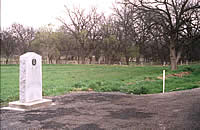 The 1936 Texas State Centennial marker had for years been located to the west of the mission site near Menard, the true location not being known at the time the maker was installed. Following discovery of the mission site in 1994, the Texas Department of Transportation moved the marker to its present location, immediately beside the mission site. In the background is seen the thick growth of alfalfa that prevented earlier archeologists, such as Kathleen Gilmore and Shawn Carlson, from finding the site. 