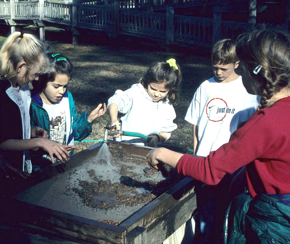 photograph of a children gathered around a screen with wet dirt on it