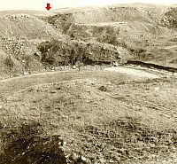 B&W photo of rugged  valley with site on flat terrace in mid-ground.