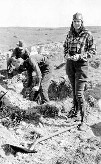 Photo of outdoor work scene with young woman in foreground facing the camera.
