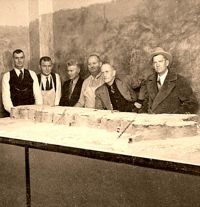 Old photo of men behind plaster model in corner of large room.