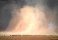 Photo of huge cloud of dust over flat fields with dark storm clouds behind it.