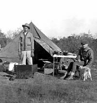 Photo of two men posing in front ofa canvas tent and touring auto and camping gear.
