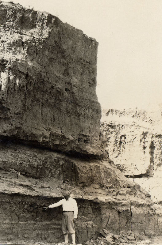 photo of Cyrus Ray pointing to a gravel layer within deeply stratified river deposits 