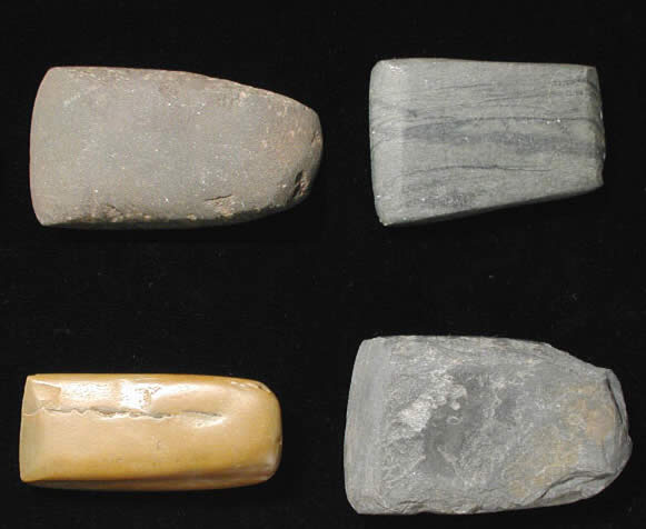 photograph of four polished stone axe heads on black background