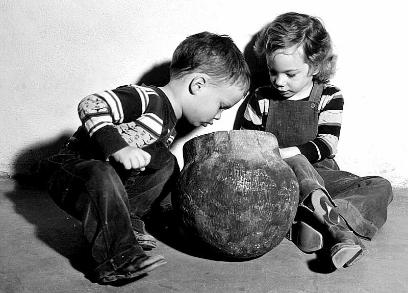  black and white photograph of two children sitting on the floor looking into a pot