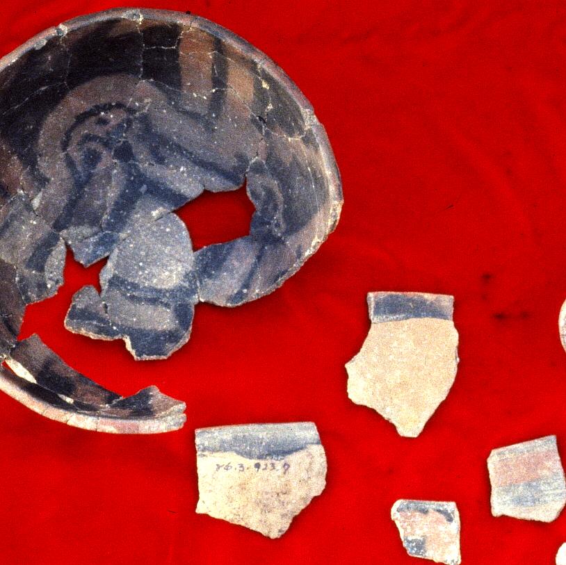 Photograph of broken grey colored pottery, some of it refit to form a portion of a bowl, on a red background.